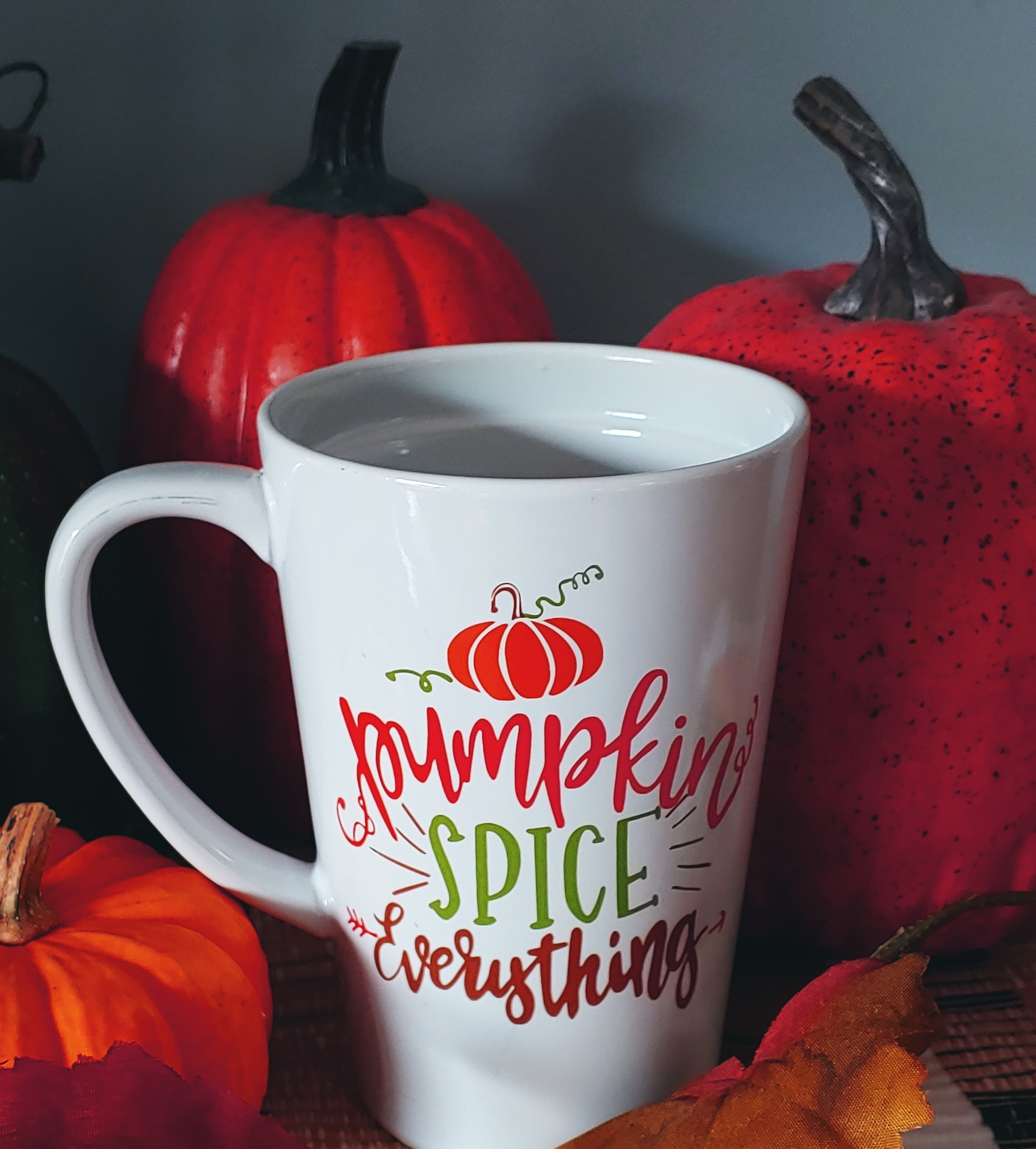 A picture of a coffee mug that says, "pumpkin spice everything" surrounded by pumpkins